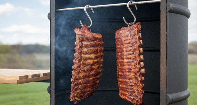 Ribs hanging from stainless hooks inside a smoker