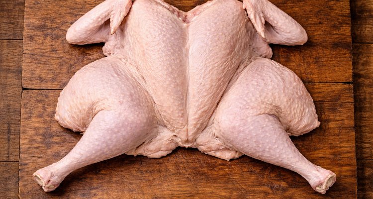 Uncooked turkey pressed completely flat in a butterfly shape on a wooden cutting board.