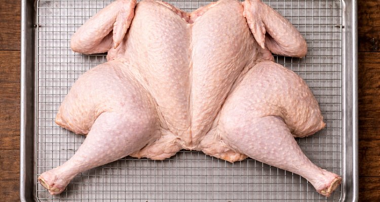 Raw spatchcocked turkey centered on a silver wire rack inside a rimmed baking sheet