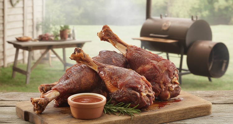 Two mahogany-brown smoked turkey legs on a rustic cutting board showing juicy pink cured meat and glossy smoked crust