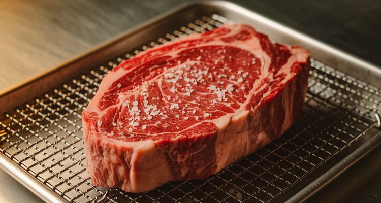 Salted ribeye steak resting on a wire rack before grilling