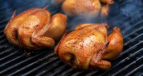 Cornish hens smoking on grill grates with thin blue smoke