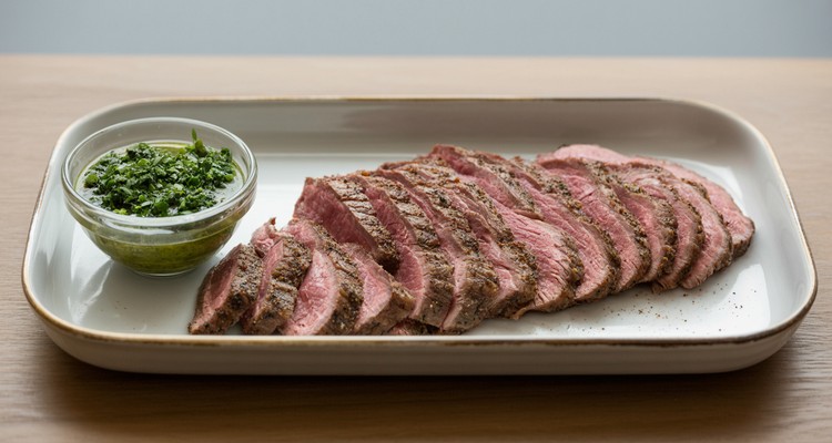 Thinly sliced smoked flank steak on a platter with chimichurri sauce