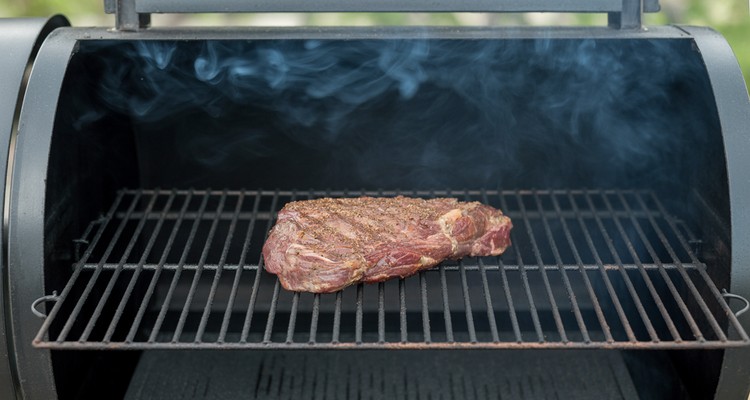 Seasoned flank steak smoking on pellet grill grates