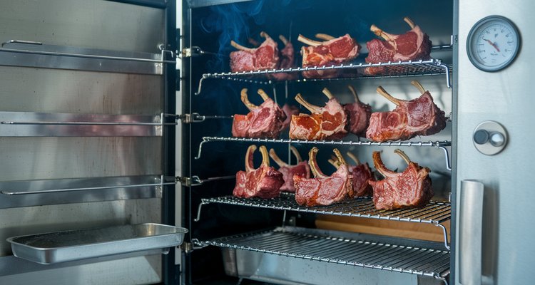 Lamb chops smoking on racks inside a vertical cabinet smoker