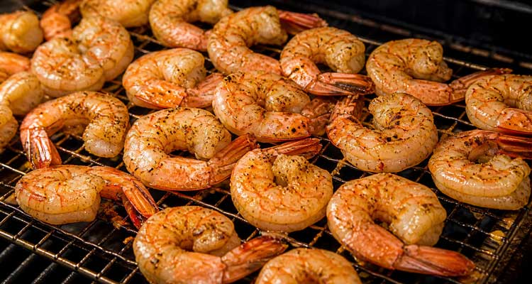 Plump pink smoked shrimp on a wire rack over smoker grates with garlic butter glaze and seasoning