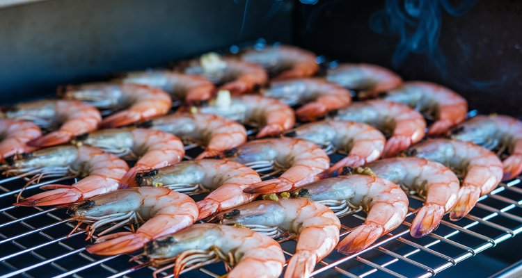 Plump pink smoked shrimp on a wire rack over smoker grates with garlic butter glaze and seasoning