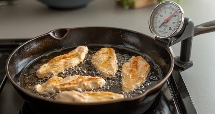 Fried chicken strips frying in a cast iron skillet with a thermometer monitoring the oil