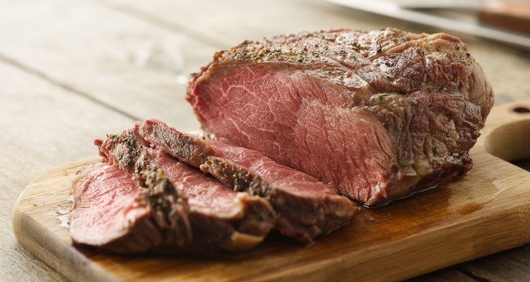 Sliced beef chuck steak on a rustic wooden cutting board showing a juicy medium-rare interior