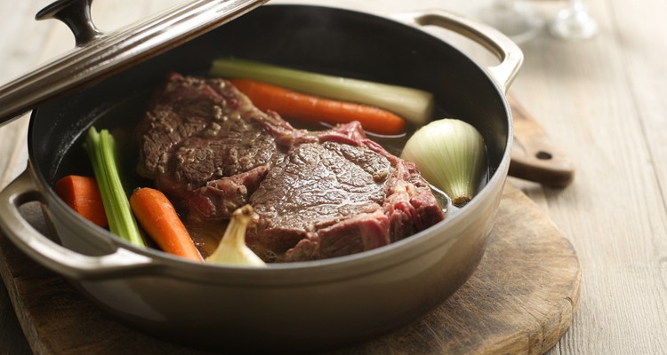 Dutch oven with the lid off showing chuck steak braising in dark liquid with carrots, onion, and celery