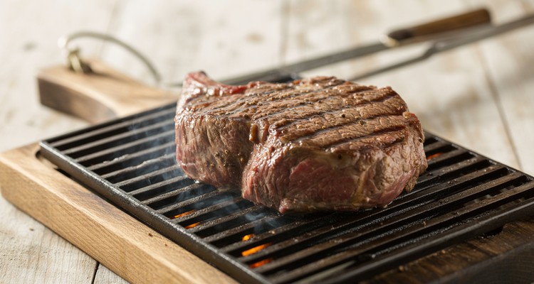 Beef chuck steak on a hot grill grate with dark sear marks and visible sizzle