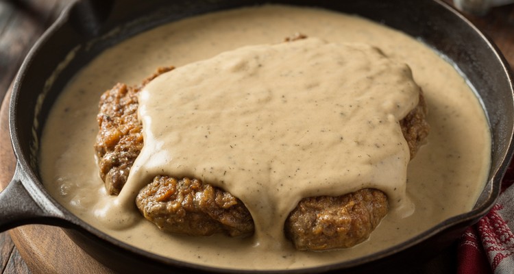 Country Fried Steak with Cream Gravy in Skillet Country fried steak in a cast iron skillet covered with creamy white pepper gravy