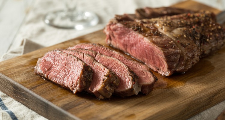 Sliced New York strip steak on a cutting board showing a juicy medium-rare center