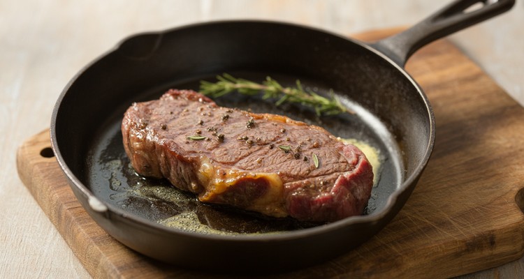 New York strip steak searing in a cast iron skillet with butter and herbs