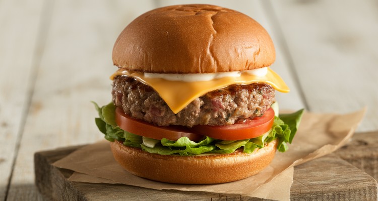 A juicy beef and pork burger on a toasted brioche bun with melted cheddar cheese, lettuce, and tomato on a rustic wooden surface