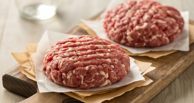 Perfectly formed raw beef and pork burger patties on parchment paper with dimples pressed in the center