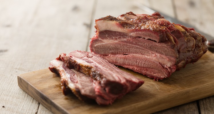 Sliced smoked beef rib meat on a wooden cutting board showing a dark bark and smoke ring