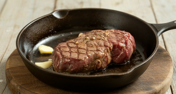 Sirloin steak searing in a cast iron skillet with butter and garlic