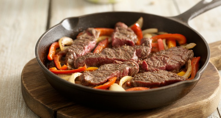 Sizzling sirloin steak strips with bell peppers and onions in a cast iron skillet