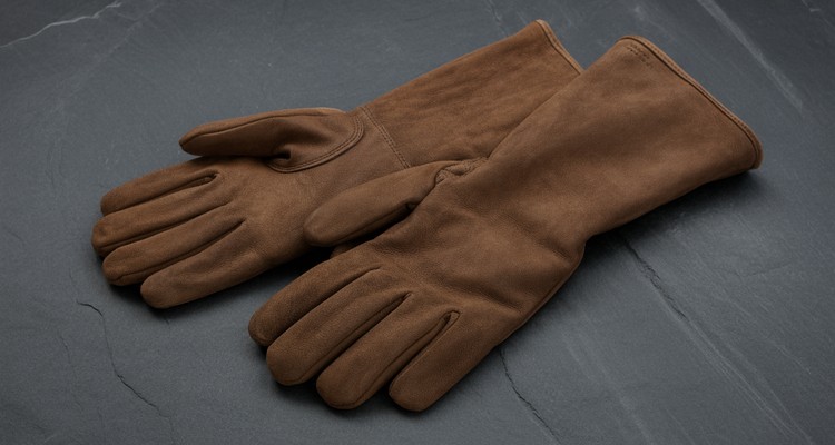 Pair of plain dark brown long cuff leather fireproof gloves on a dark slate surface
