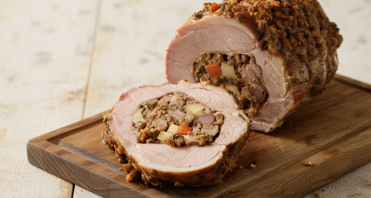 Sliced stuffed pork loin showing apple sausage stuffing on a dark wood cutting board