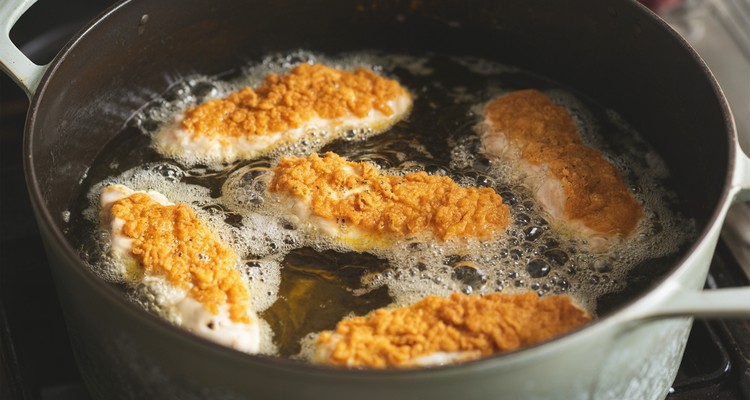 Breaded chicken strips frying in hot oil in a Dutch oven