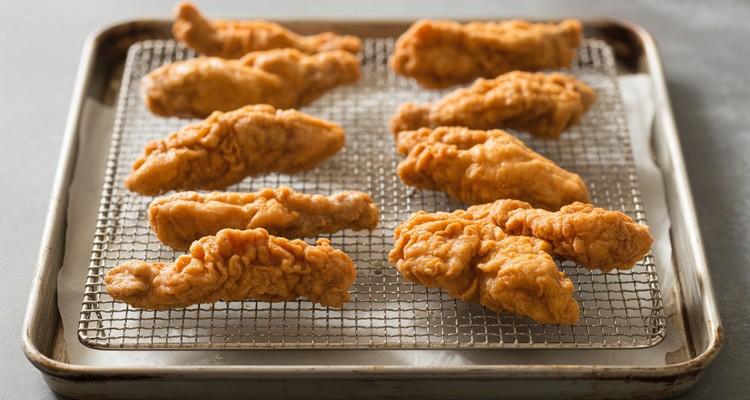 Crispy fried chicken fingers draining on a wire rack over a baking sheet