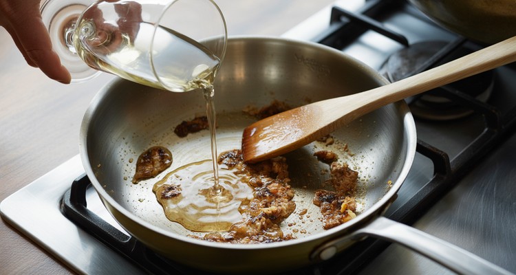 White wine being poured into skillet with fond to deglaze for chicken piccata sauce