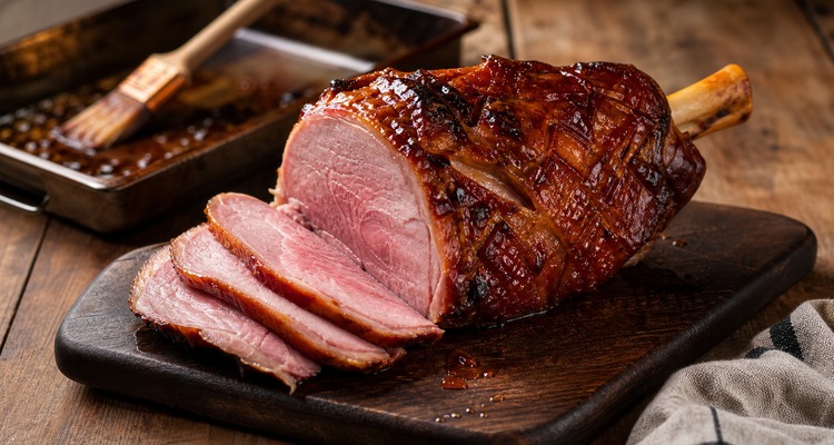 Glazed bone-in ham shank sliced on a cutting board