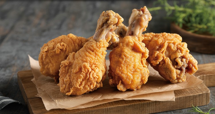 Crispy golden fried chicken drumsticks stacked on a wooden board