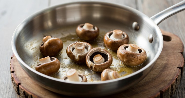 Cremini mushrooms browning in a stainless steel skillet until golden with fond developing on the pan bottom