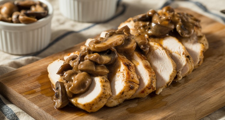 Sliced grilled chicken breast topped with glossy brown marsala sauce and mushrooms on a rustic plate