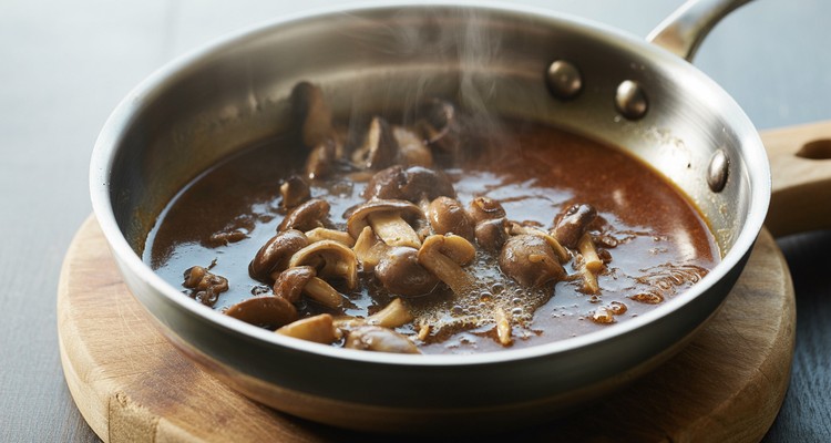 Marsala sauce reducing in a stainless steel skillet with browned mushrooms, steam rising, and fond dissolving into the sauce