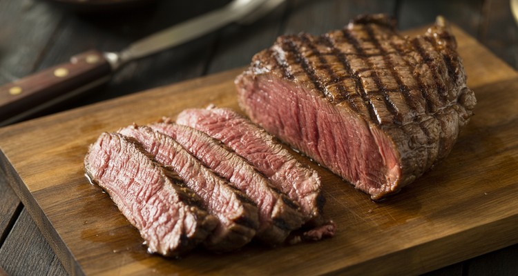 Perfectly grilled sirloin tip steak sliced against the grain showing a rosy medium-rare interior on a wooden cutting board with visible grill marks