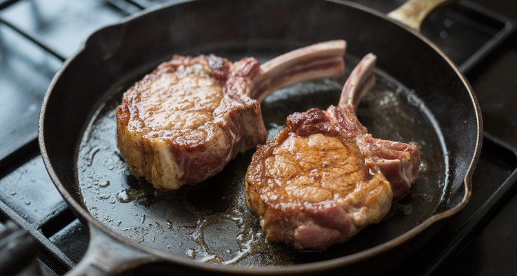 Two thick pork chops searing in a hot cast-iron skillet with a deep golden-brown crust and oil sizzling around them