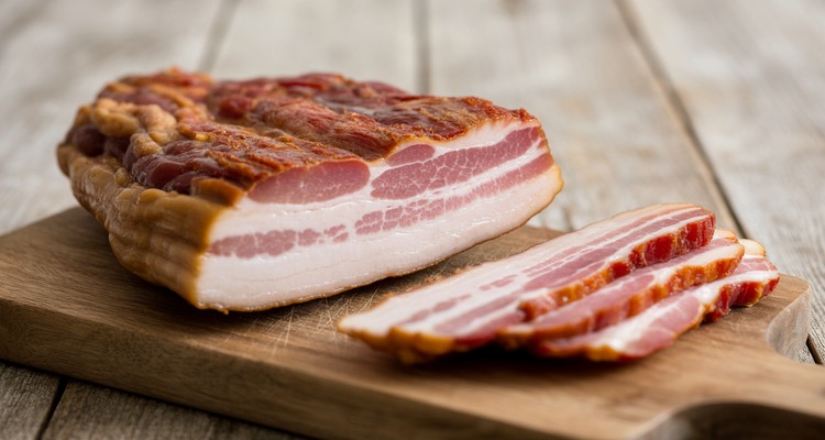 Sliced smoked pork jowl bacon on a wooden cutting board with a mahogany crust