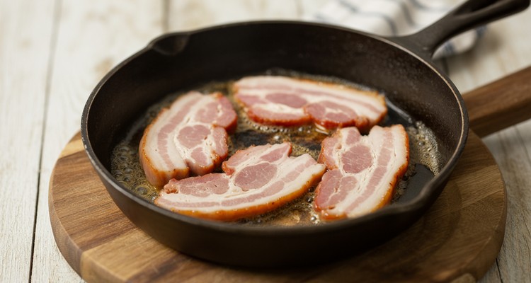 Pork jowl bacon slices sizzling in a cast iron skillet with rendered fat