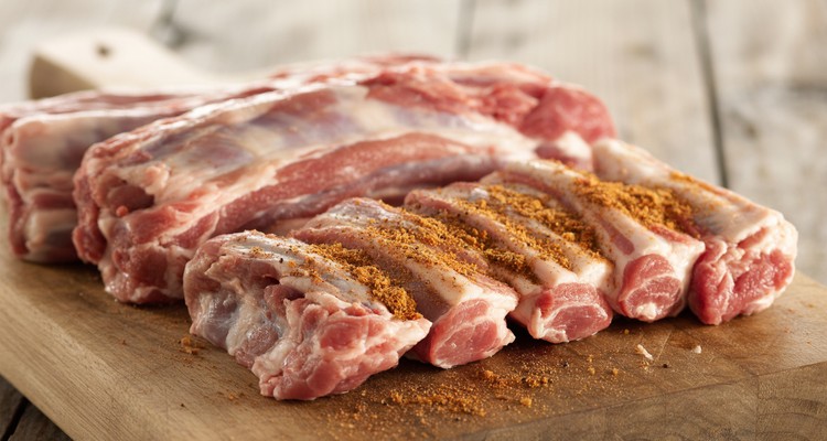 Raw pork riblets being seasoned with dry rub on a cutting board