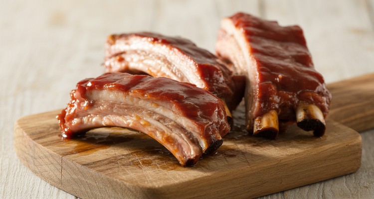 Smoked pork riblets with glossy BBQ sauce glaze on a rustic wooden cutting board