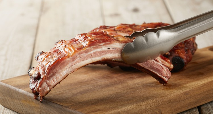 The Bend Test for Rib Doneness Tongs holding rack of smoked pork ribs showing bend test crack in bark for doneness