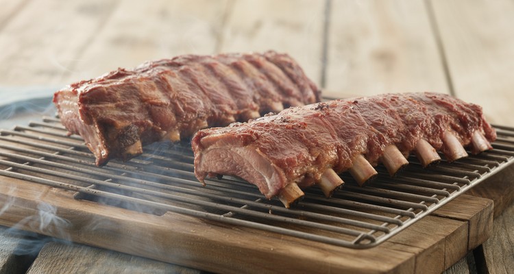 Smoked Pork Ribs on the Smoker Two racks of pork ribs on smoker grates with mahogany bark forming and wisps of smoke