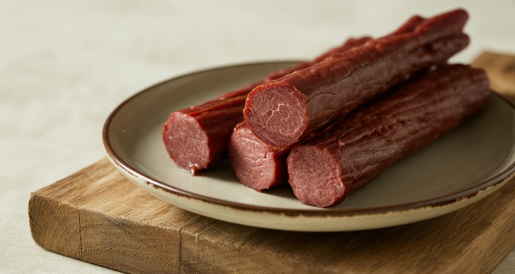 Close up of sliced smoked beef sticks showing firm reddish interior on a plain plate