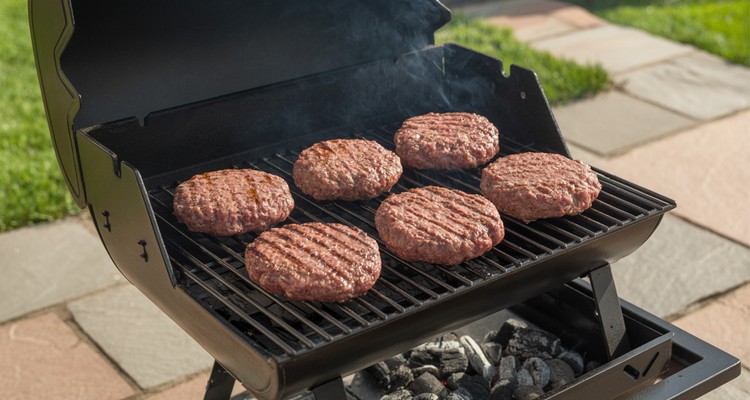 Smoked burger patties on a grill grate showing deep smoky color before the final sear