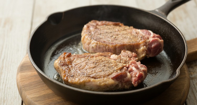 Pan-Searing Pork Steaks for Smothered Pork Steak Recipe Flour-dredged pork shoulder steaks searing in a hot cast-iron skillet with a golden-brown crust forming