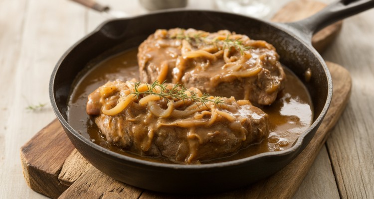 Smothered Pork Steaks in Onion Gravy Ready to Serve Smothered pork steaks simmering in rich onion gravy in a cast-iron skillet, ready to serve