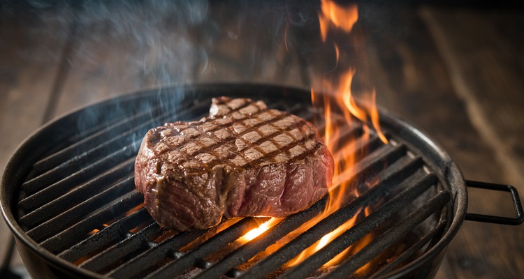 Tip steak searing over direct flames on a grill with grill marks forming on the surface