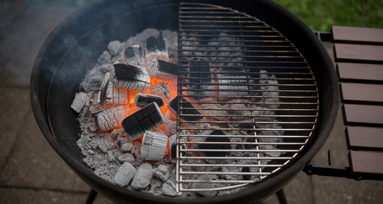 Two-zone charcoal grill setup showing hot coals banked on one side and empty grate on the other for indirect cooking
