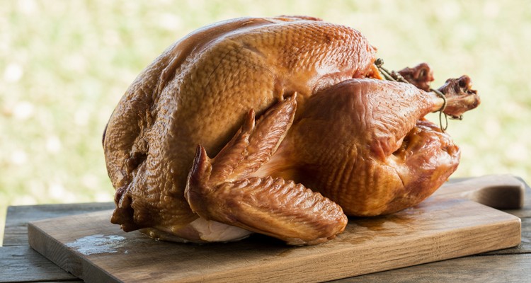 Whole smoked turkey resting on a rustic wooden carving board with golden-brown crispy skin